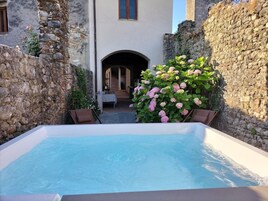 Jacuzzi en un patio con paredes de piedra y vista a un edificio.