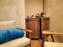 Una habitación pequeña con un sofá, un mueble de madera con una tetera y una silla.