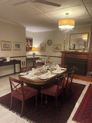 Une salle à manger avec une table ronde dressée pour un repas, entourée de chaises, d’un lustre et d’œuvres d’art encadrées accrochées aux murs.