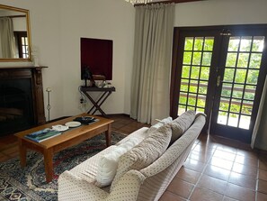A living room with a sofa, a coffee table, a fireplace, a mirror, and a view through a door. - Secluded Chalet Retreat near Kruger Park, Luxury Meets Nature, Farm living (Kiepersol)