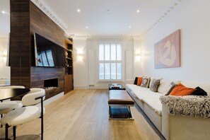A modern living room with a flat-screen TV, a sofa, a coffee table, and a fireplace. - Luxury 3BDR Chelsea Townhouse Sleeps 6 (London)