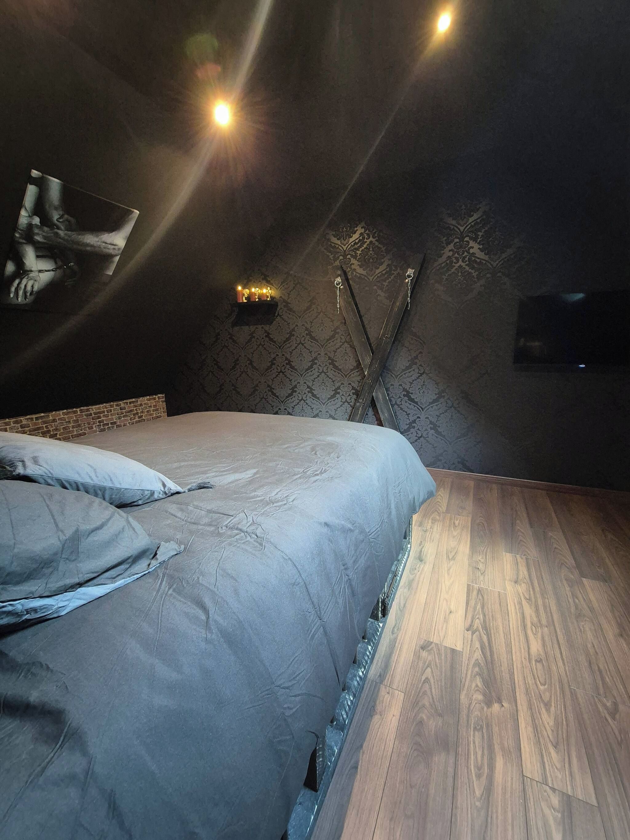Une chambre à coucher avec un lit, un plancher en bois, un téléviseur fixé au mur et une étagère avec des bougies.