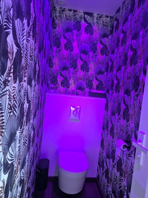 Un baño con inodoro, un cubo de basura y una pared con diseño de hojas.