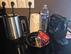 Una cocina con cafetera, hervidor de agua, botella de agua, rollo de toallas de papel y máquina de café.