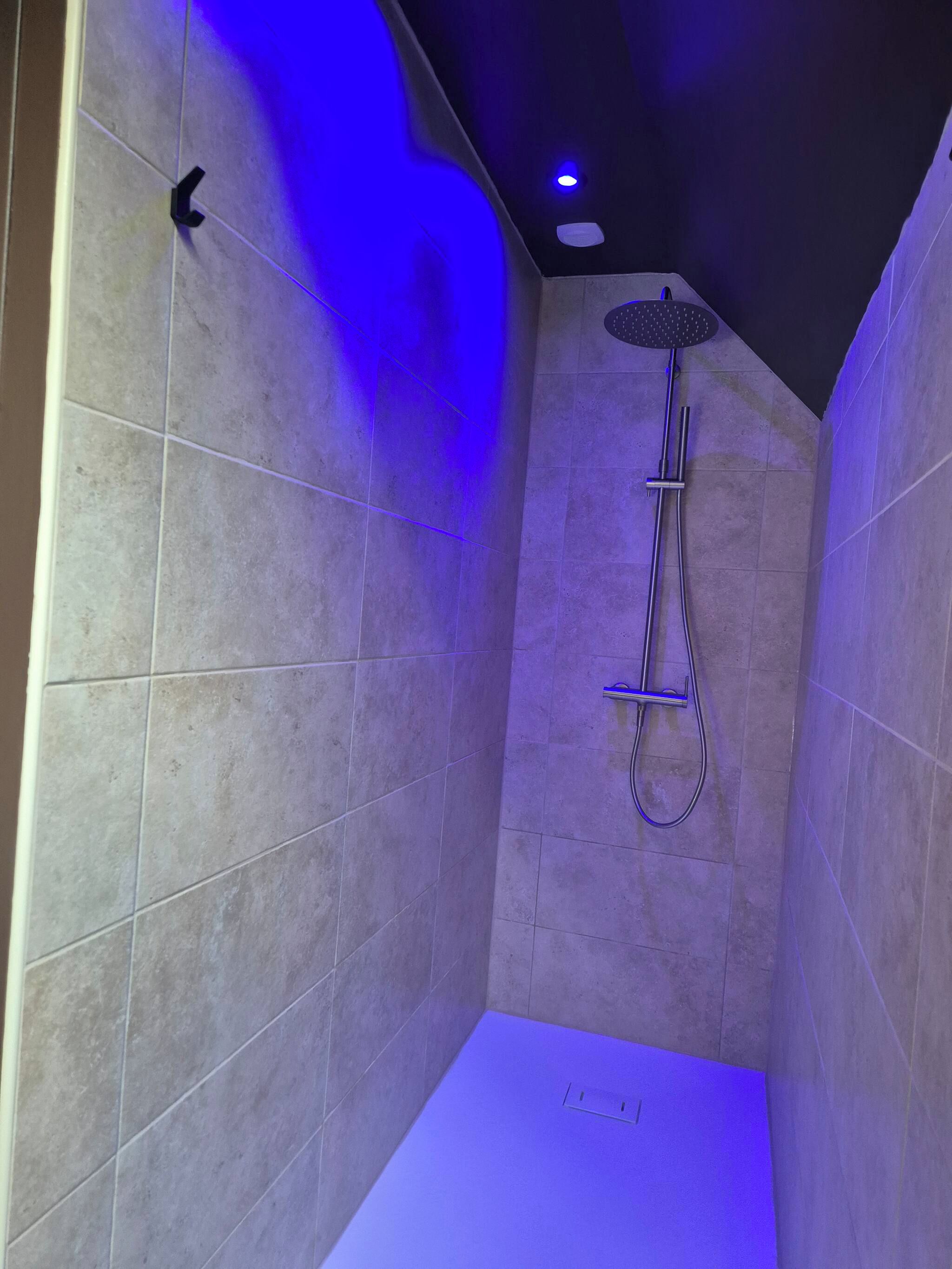 Een kleine douchekamer met betegelde wanden, een handdouche en een bedieningspaneel aan de muur.
