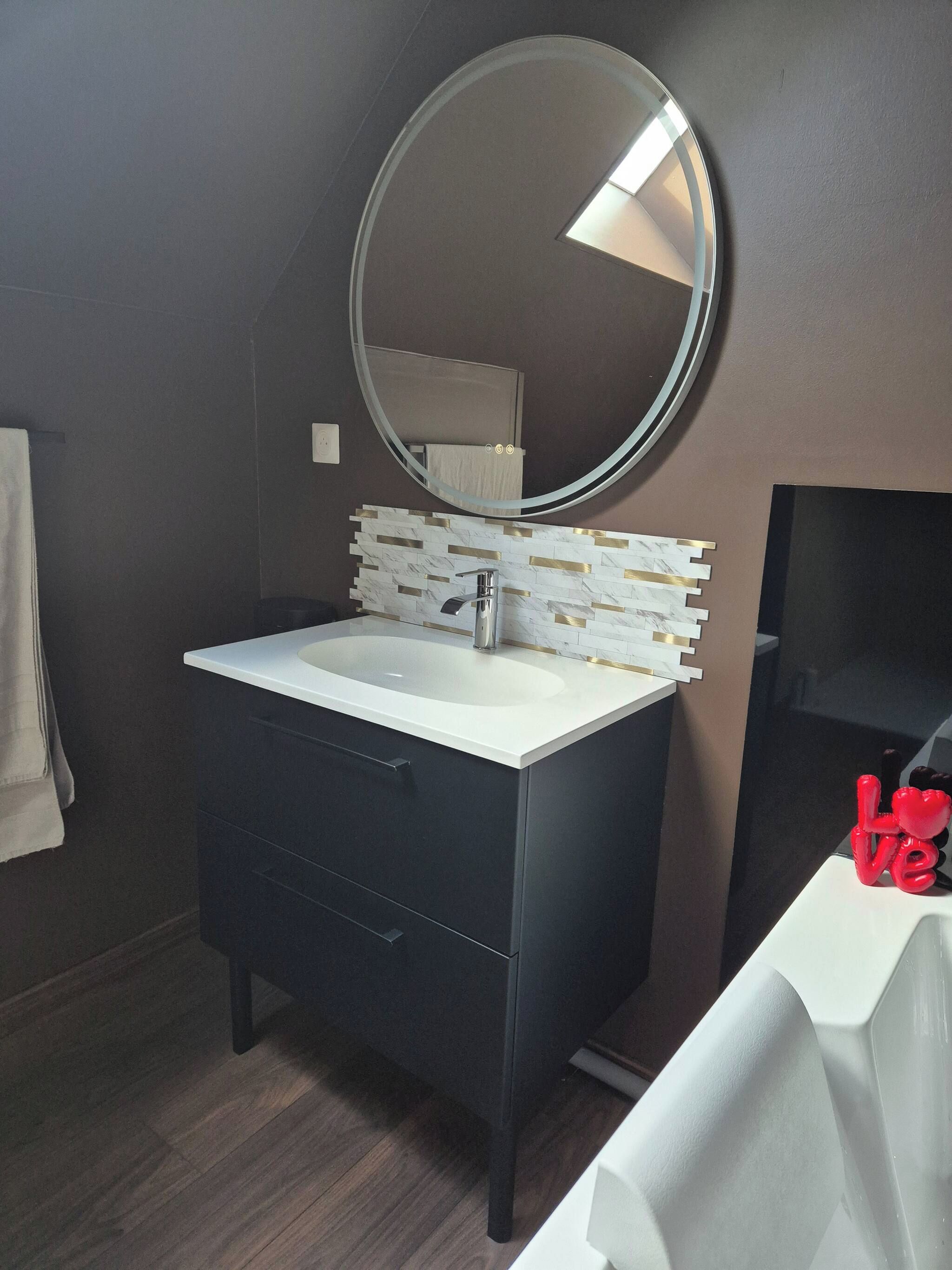 Un bagno con un mobile lavabo scuro, un lavandino bianco, uno specchio rotondo e un porta asciugamani.