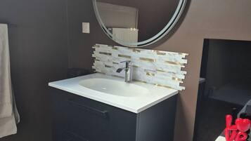 Un bagno con un mobile lavabo scuro, un lavandino bianco, uno specchio rotondo e un porta asciugamani.