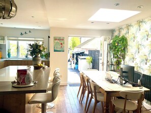 A modern kitchen with a dining area, featuring a large island with a vase of flowers, a dining table with chairs, and a view of the outside. - Beautiful House 5 mins walk into Ulverston (Westmorland and Furness)