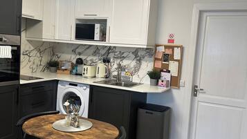 Cozinha com armários brancos, máquina de lavar, micro-ondas e cafeteira.