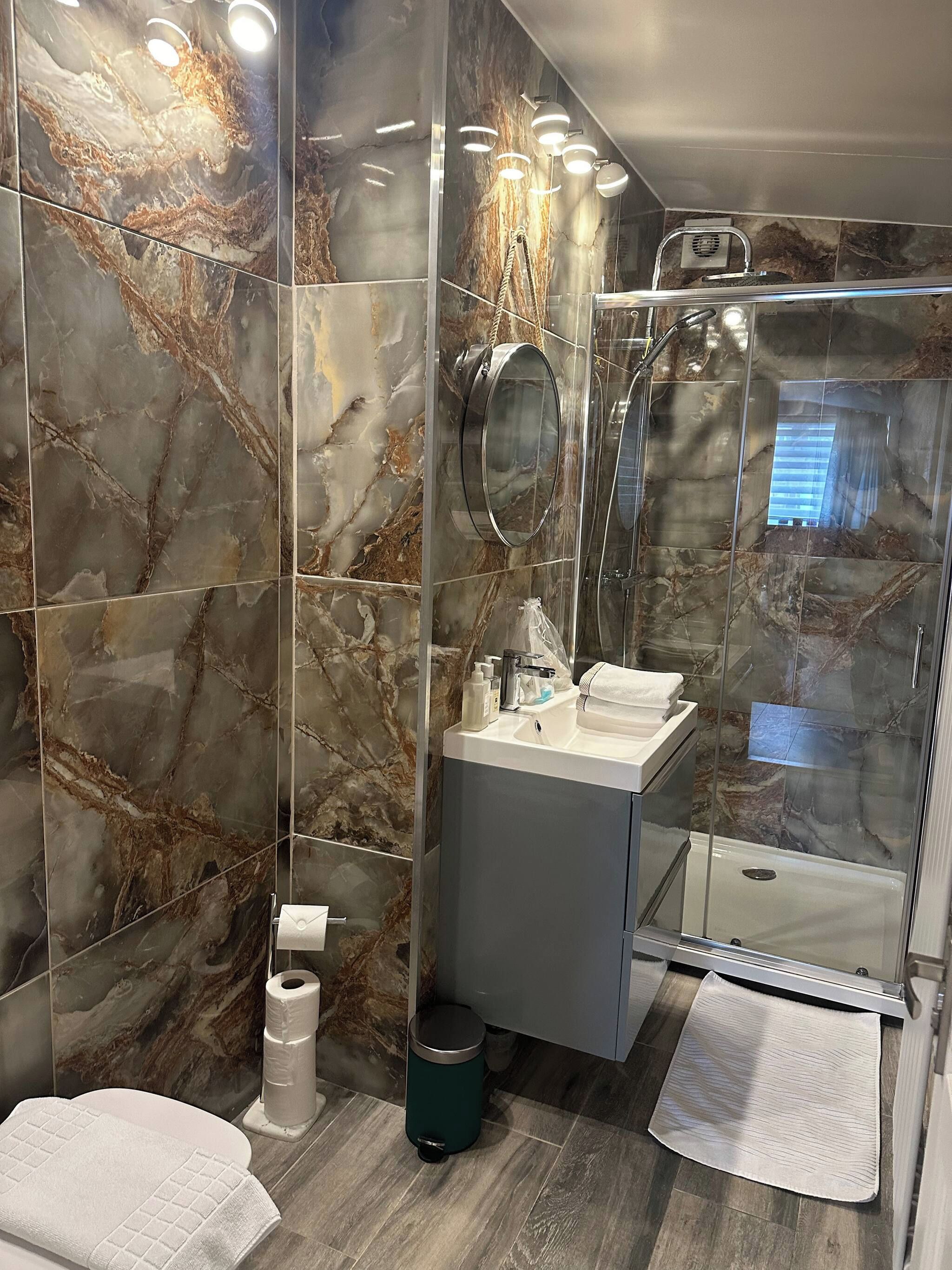 Une salle de bain moderne avec des murs en marbre, une douche en verre et un meuble-lavabo avec un miroir.