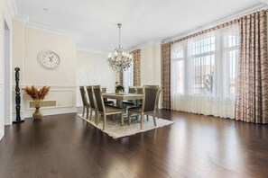 A dining room with a chandelier, a clock, and a window with curtains.