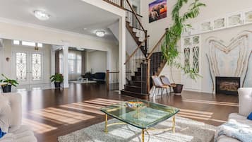 Un vaste espace de vie agrémenté d’une table basse en verre, d’un escalier et d’une grande plante.