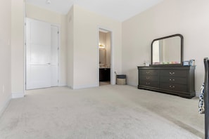 Ein Zimmer mit einer weißen Tür, einem dunklen Schminktisch mit Spiegel und einem hellen Teppich.
