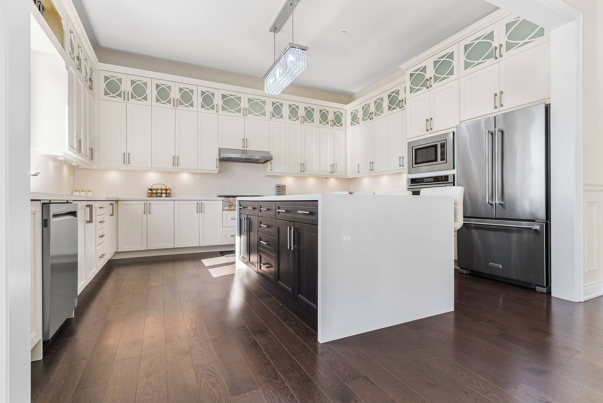 Una cocina con armarios blancos, una isla central, electrodomésticos de acero inoxidable y un techo con diseño.