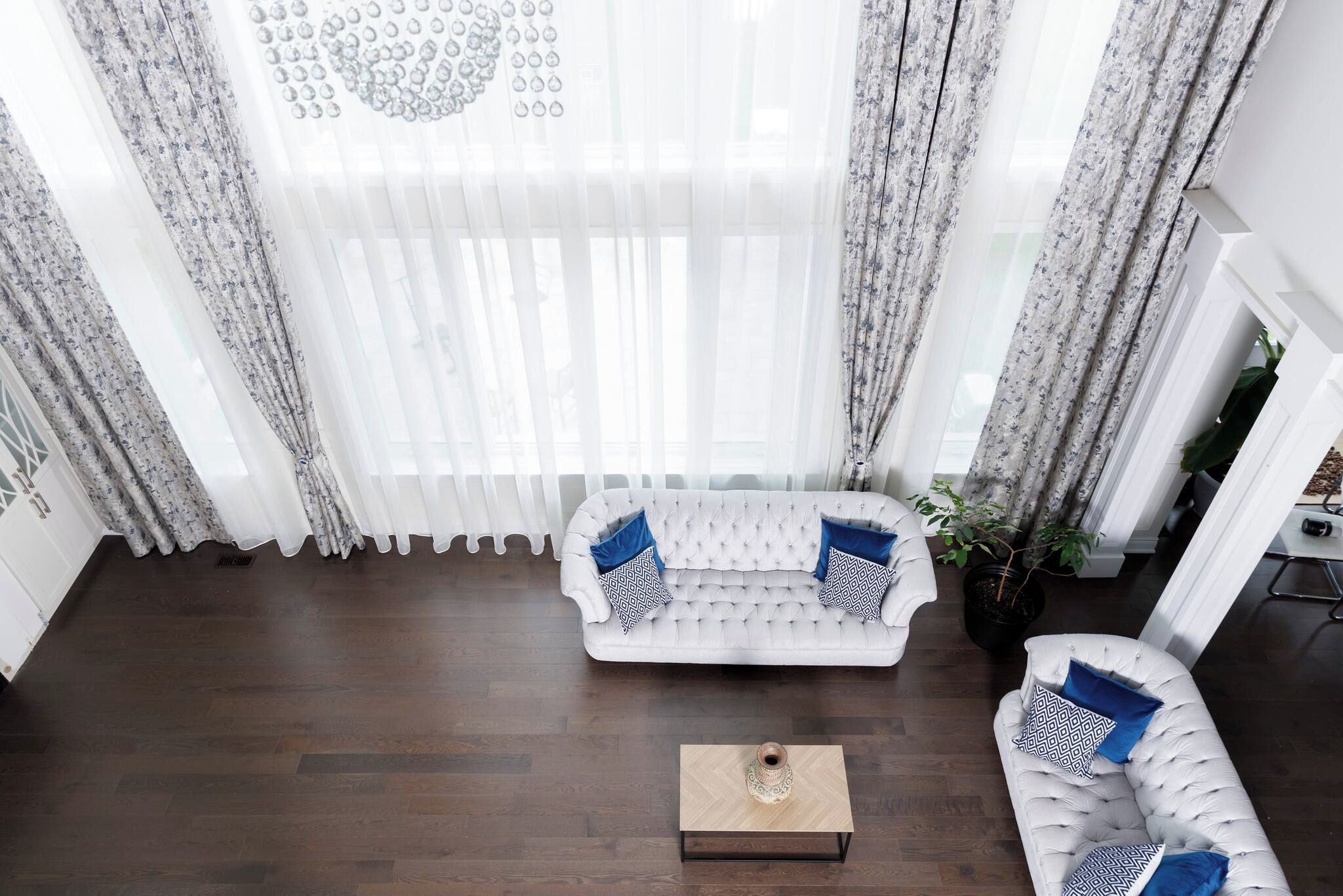 Un salon moderne avec un canapé blanc, une table basse et une grande fenêtre ornée de rideaux légers.