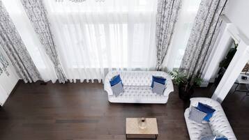 Un salon moderne avec un canapé blanc, une table basse et une grande fenêtre ornée de rideaux légers.