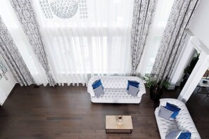 A modern living room with a white sofa, a coffee table, and a large window with sheer curtains.