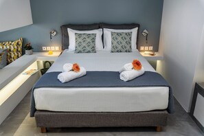A neatly made bed with two towels and flowers, a grey upholstered headboard, and a bedside table with a lamp and a small potted plant. - Amara Solar Living Ground Apartment (Agia Marina)