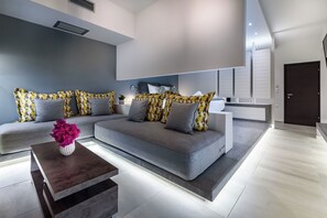 Ein modernes Wohnzimmer mit einer grauen Sofagarnitur, gemusterten Kissen, einem kleinen Tisch mit einer Vase und einem minimalistischen Design.