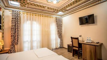 A hotel room with a bed, a desk, a chair, curtains, and a television.