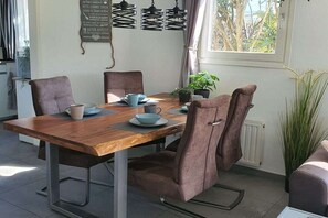 A dining area with a wooden table, four chairs, and a window with a view of trees. - Stella Zeeland Beachhouse (Kamperland)