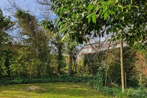 A lush garden with a variety of trees and shrubs, a grassy lawn, and a fence. - Stella Zeeland Beachhouse (Kamperland)