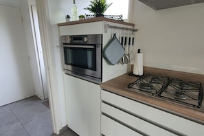 Ett kök med en inbyggd ugn, en gasspis och köksredskap som hänger upphängda.