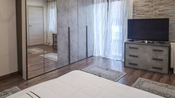 Une chambre à coucher avec un grand lit, une armoire avec un miroir, un téléviseur posé sur un meuble et une fenêtre avec des rideaux.