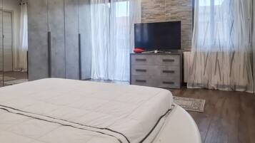 Une chambre à coucher avec un grand lit, un téléviseur à écran plat, une commode et une fenêtre ornée de rideaux légers.