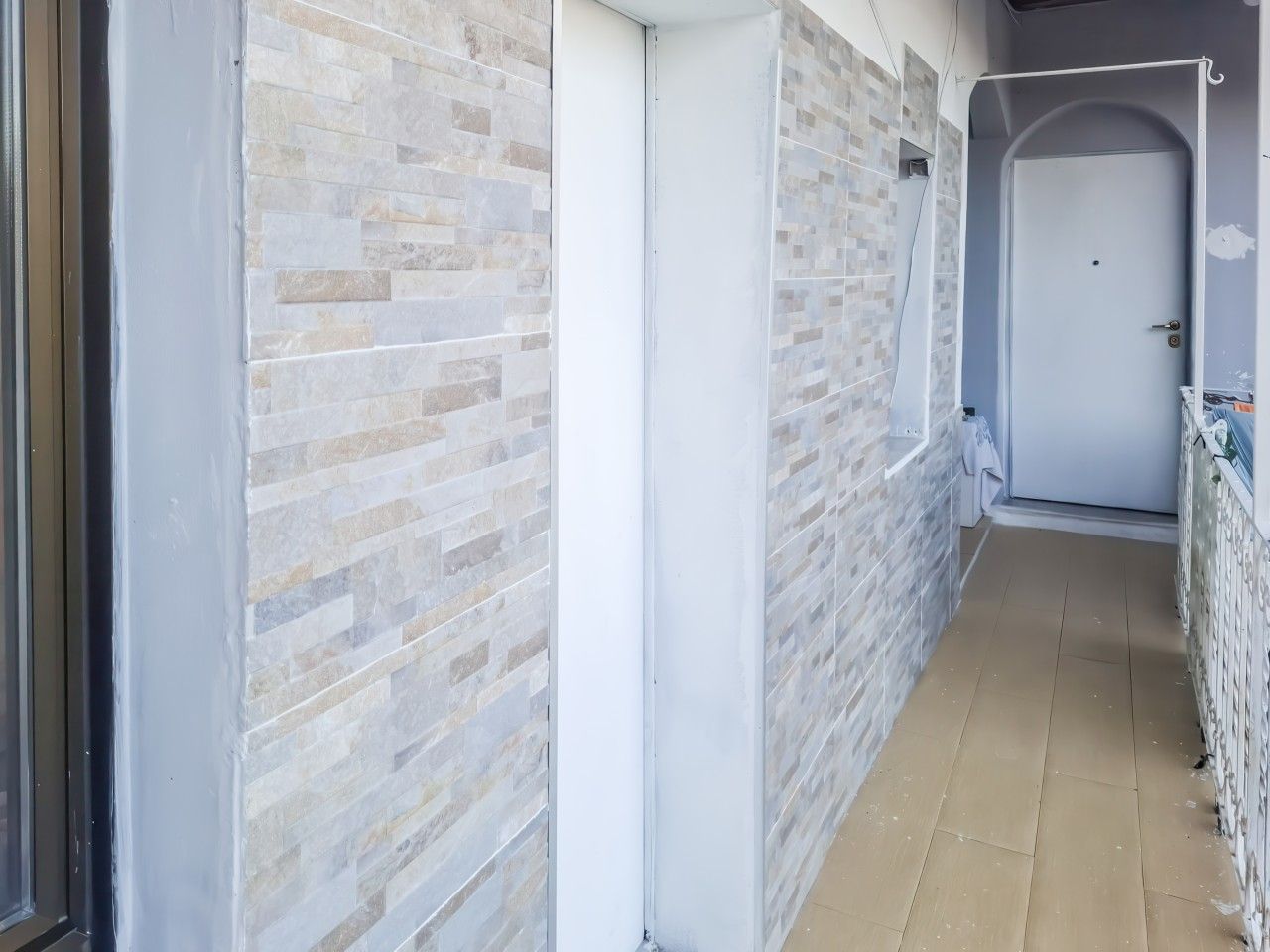 Un couloir avec un mur recouvert de carreaux, une porte fermée et une prise électrique visible.