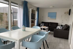 A dining area with a white table and blue chairs, a brown sofa, and a small white table with a basket. - Type A "Zee, Bos en Duin" Zoutelande (Zoutelande)