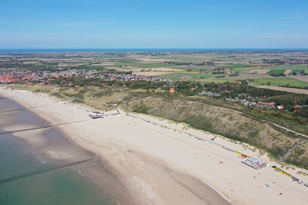 Vista aérea de una zona costera con playa, un pueblo pequeño y campos abiertos.