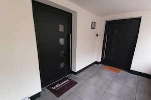 A hallway with two black doors, a welcome mat, and a small wall-mounted light fixture. - FeWo Excellence Juwel (Cochem)