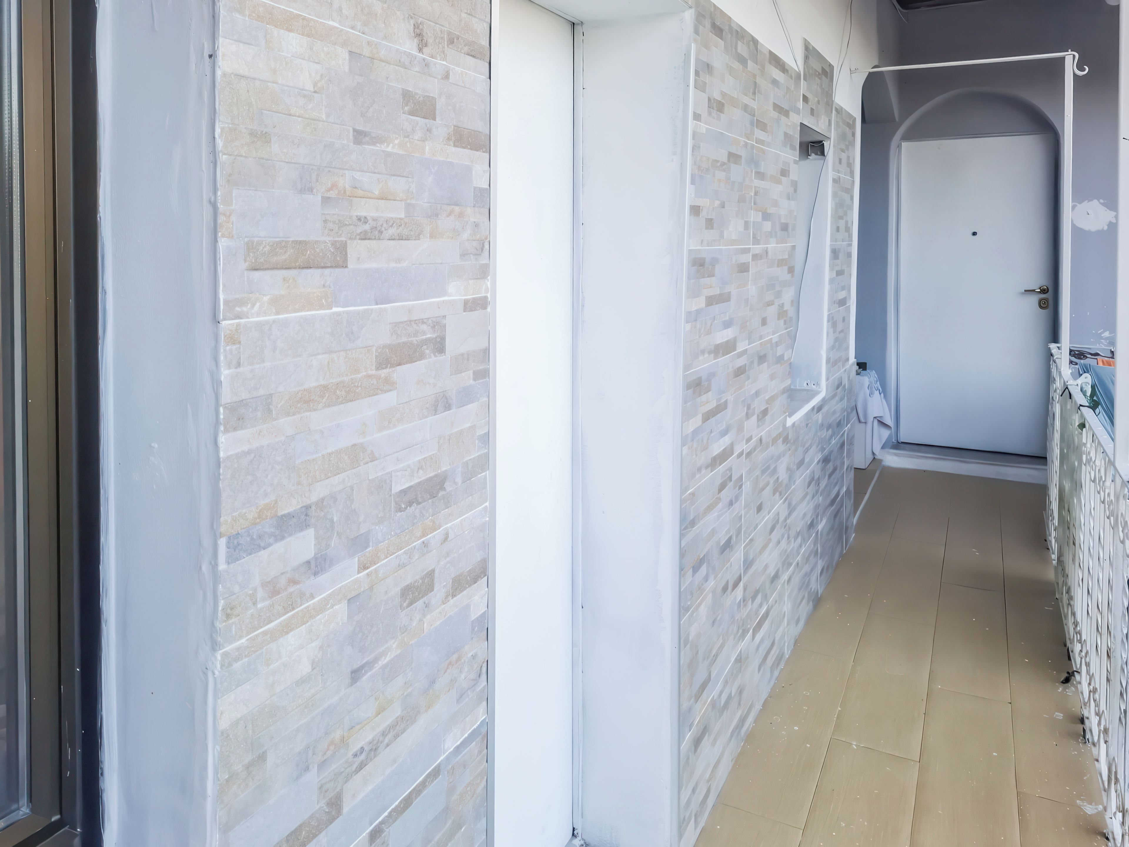 Un couloir avec un mur recouvert de carreaux, une porte blanche et un sol carrelé.