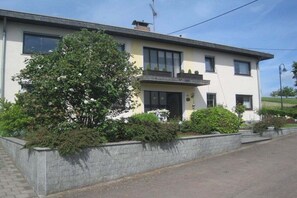 A two-story house with a front porch, a large tree, and a stone retaining wall. - Holiday apartment with 2 bedrooms (Henschhausen)