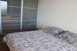 Una camera da letto con un letto, un comodino e un'ampia finestra con persiane.