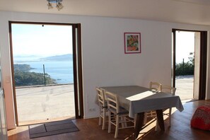 Ein Essbereich mit Tisch und Stühlen, Blick auf das Meer durch ein großes Fenster und eine Tür, die nach draußen führt.
