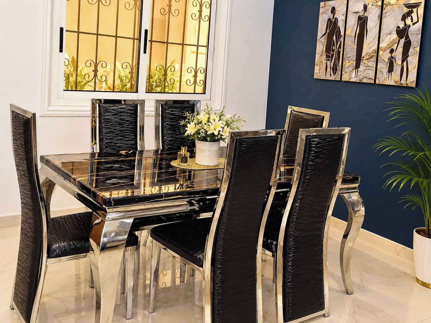 A dining area with a glass-top table, black upholstered chairs, and a decorative vase with flowers.