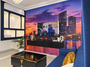 A modern living room with a cityscape mural, a black entertainment unit, and a blue sofa. - 4 Bedroom Villa Duplex Abidjan Cocody Riviera•Secured•2 Grandes terraces•WIFI•AC (Abidjan)