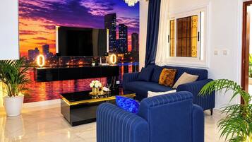 A modern living room with a cityscape mural, a flat-screen TV, a sofa, a coffee table, and a chandelier.
