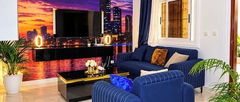 A modern living room with a cityscape mural, a flat-screen TV, a sofa, a coffee table, and a chandelier.