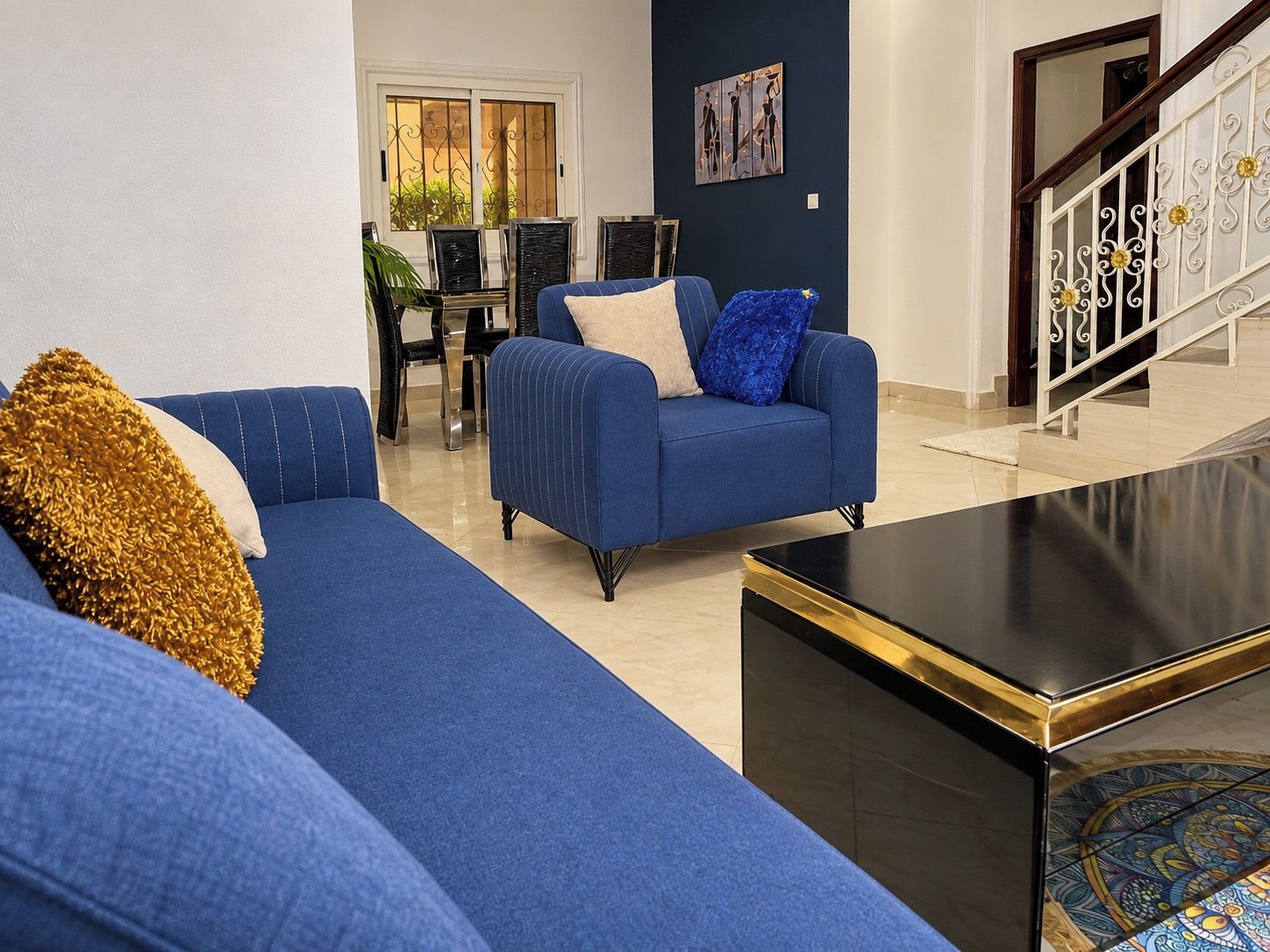 A living room with a blue sofa, a black coffee table, and a staircase with white railings.