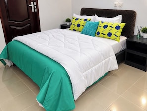 A neatly made bed with a green and white duvet, a dark headboard, and a bedside table with a small plant and a lamp. - 4 Bedroom Villa Duplex Abidjan Cocody Riviera•Secured•2 Grandes terraces•WIFI•AC (Abidjan)