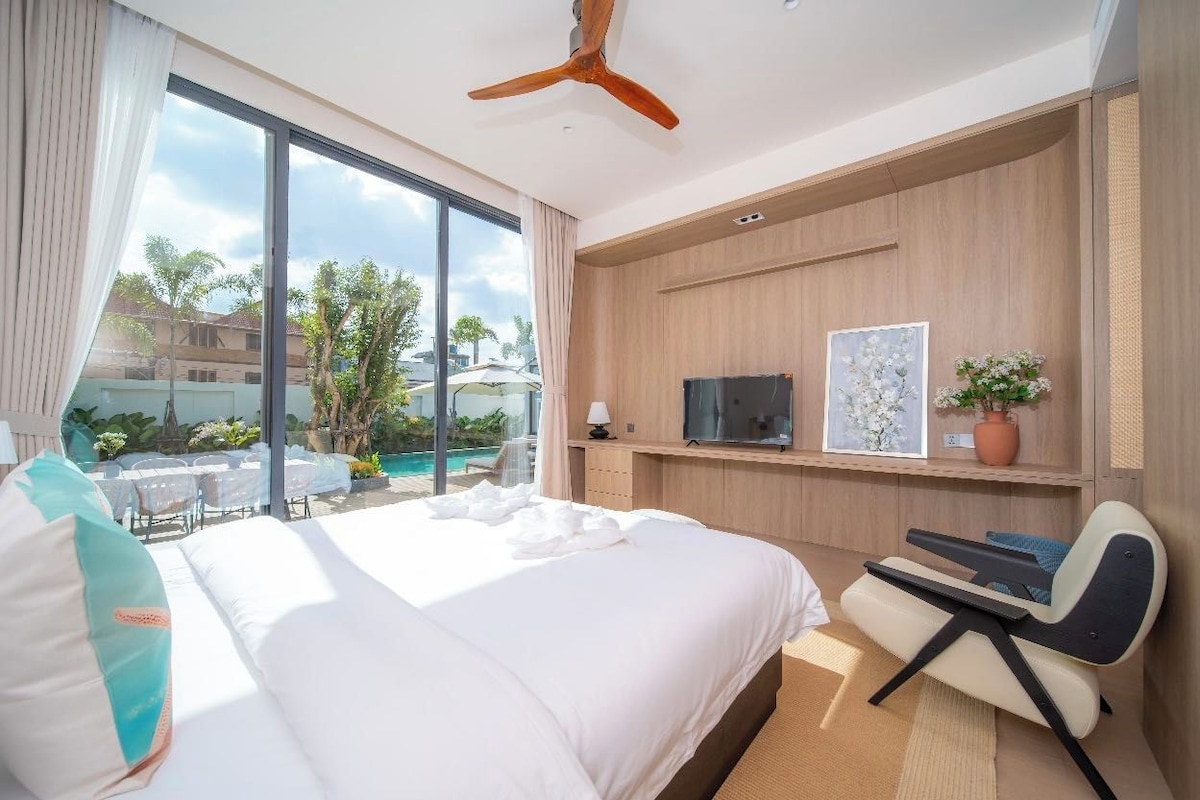A hotel room with a large bed, a desk, a television, and a view of a pool and outdoor area.