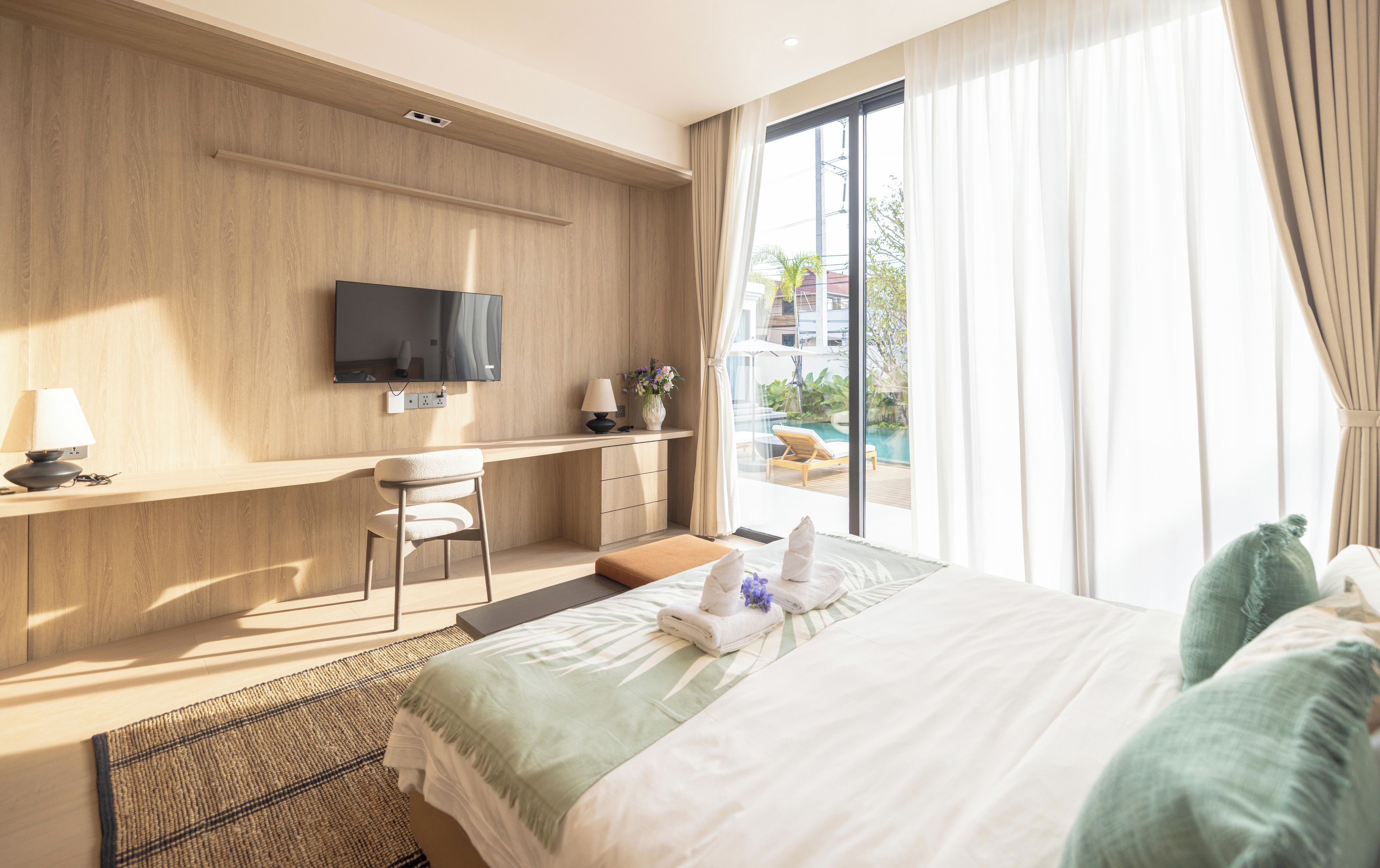 Une chambre d’hôtel équipée d’un lit, d’un bureau, d’une chaise, d’un téléviseur fixé au mur et offrant une vue sur une piscine.