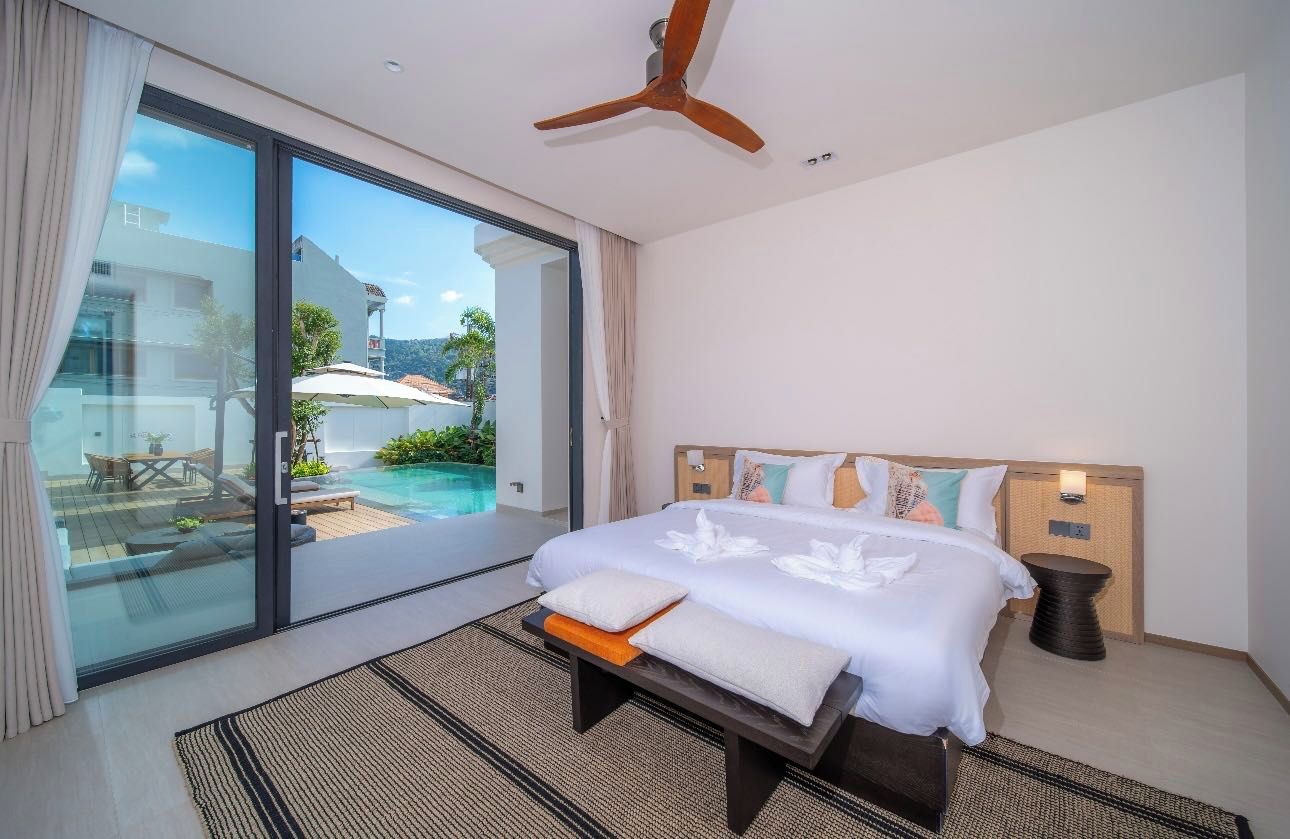 Une chambre d’hôtel comprenant un lit, une table de chevet, un ventilateur de plafond et donnant sur une piscine extérieure et un patio.