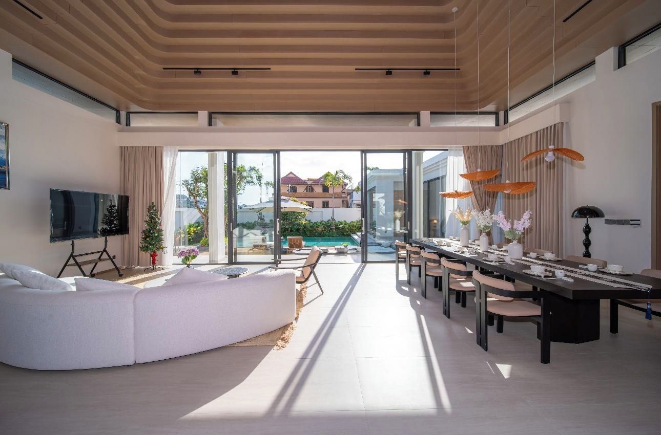 Un salon moderne avec un grand canapé, un téléviseur à écran plat et un coin repas comprenant une longue table et des chaises.