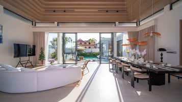 Un salon moderne avec un grand canapé, un téléviseur à écran plat et un coin repas comprenant une longue table et des chaises.
