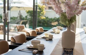 Mesa de comedor dispuesta con cuencos, palillos y un florero, con vista a asientos al aire libre y follaje.