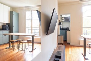A modern kitchen with a flat-screen TV mounted on the wall, wooden flooring, and a dining area with bar stools. - Central and Bright 1BDR Apartment near Notre Dame (Paris)